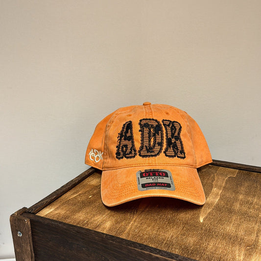 Orange cap with 'ADK' branding on a wooden surface